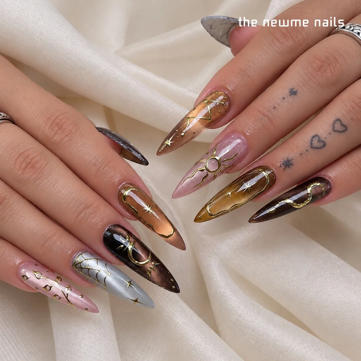Long stilettos in pink, silver, amber, copper and black chrome, drawn in raised gold line work with suns, stars, a crescent moon, a spider web and winding vines.