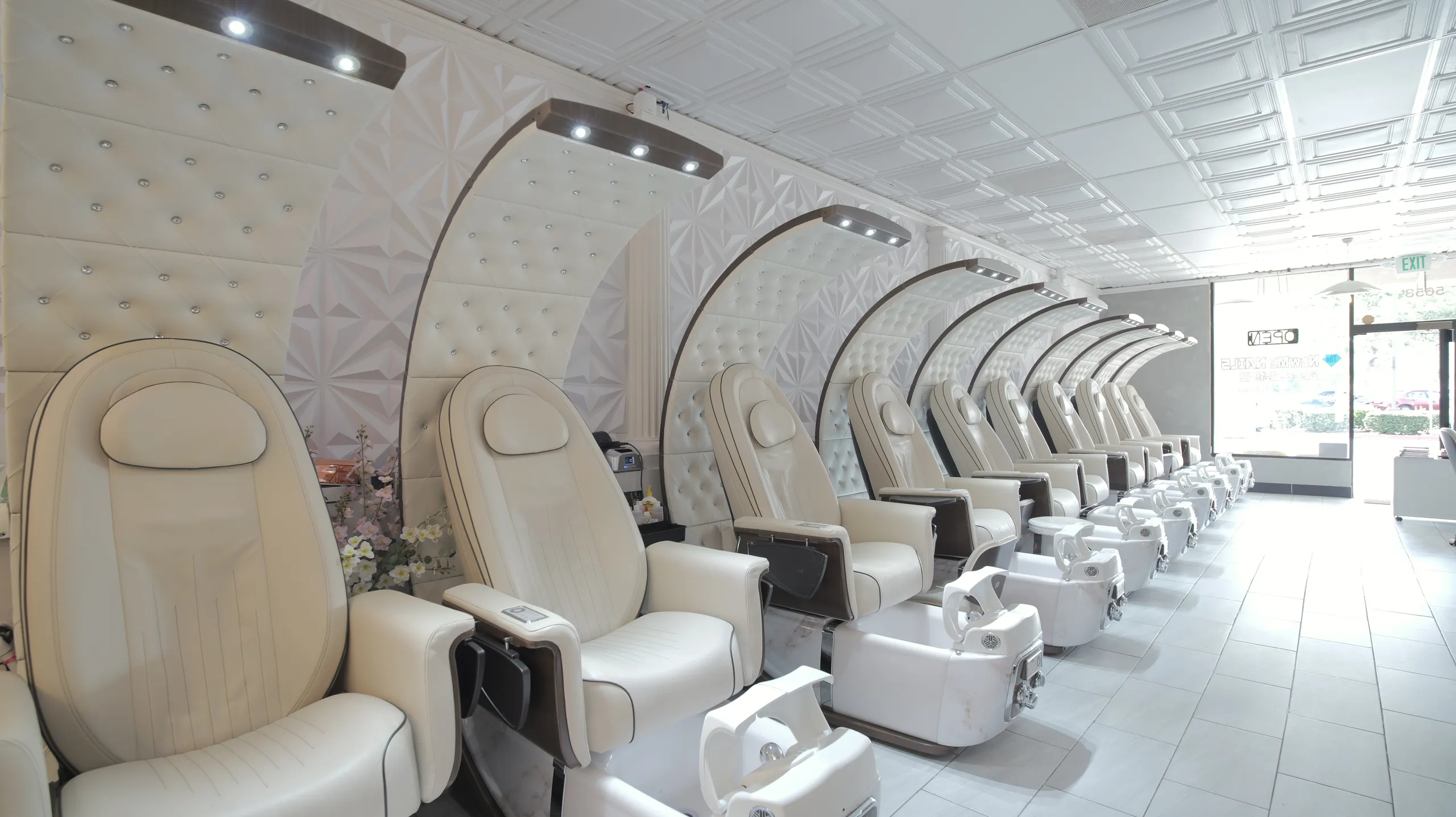 A row of cream pedicure chairs with tall arched backs along a bright white studio wall.